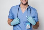 cheerful man doctor in uniform standing with stethoscope in light room
