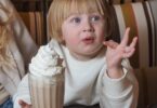 photo of a blond baby having hot chocolate with whipped cream