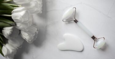 white gua sha tools placed near bouquet of flowers on marble table