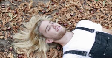 man in white shirt lying on brown dried leaves