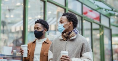 black men in medical masks with takeaway coffee on street