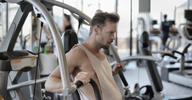 strong sportsman exercising with shoulder press machine in gym