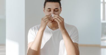 sick man in white shirt wiping his nose with tissue
